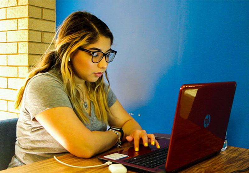 女学生坐在书桌前看着一台红色的笔记本电脑