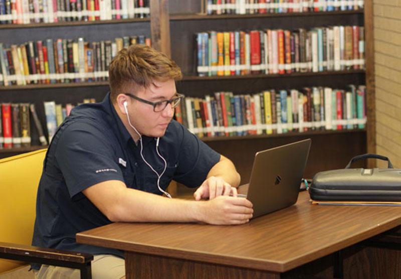 在图书馆用笔记本电脑学习的男生